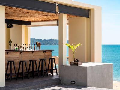 Bar sulla spiaggia aperta con sgabelli di legno e vista sul mare azzurro sotto un cielo sereno.