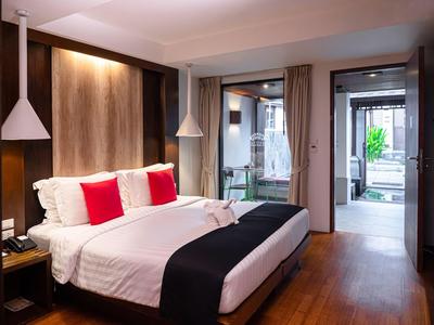Modernes Hotelzimmer mit großem Bett, weißen und roten Kissen sowie Zugang zu einer Terrasse.