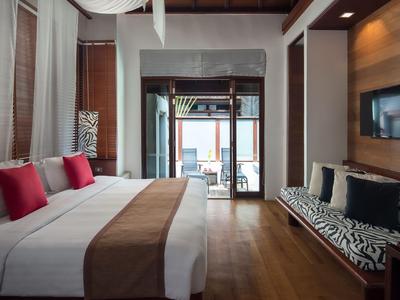 Hotelzimmer mit Doppelbett, roten Kissen und Lounge-Bereich mit Blick auf eine Terrasse.