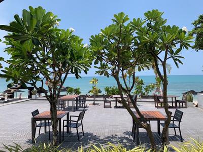 Freiluftrestaurant mit Tischen und Stühlen, umgeben von kleinen Bäumen mit Blick aufs Meer.