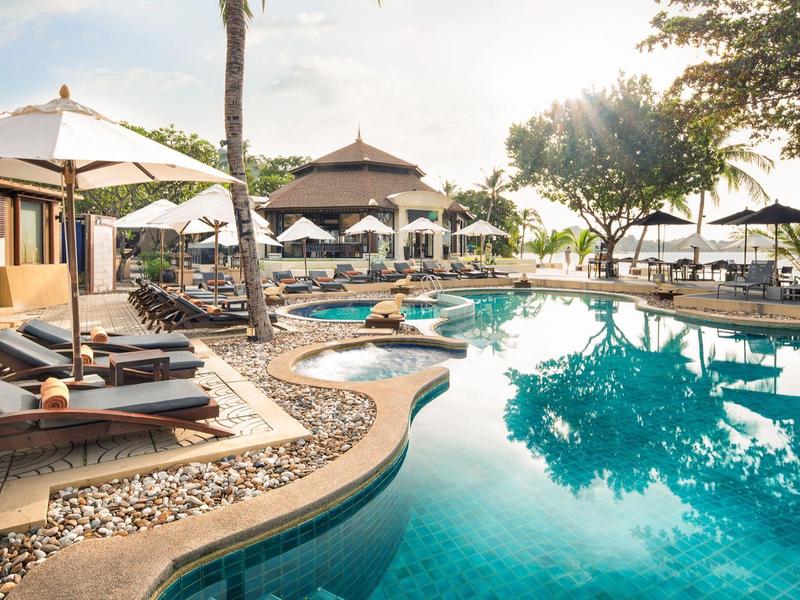 Area piscina moderna con lettini e ombrelloni in un hotel tropicale al tramonto.