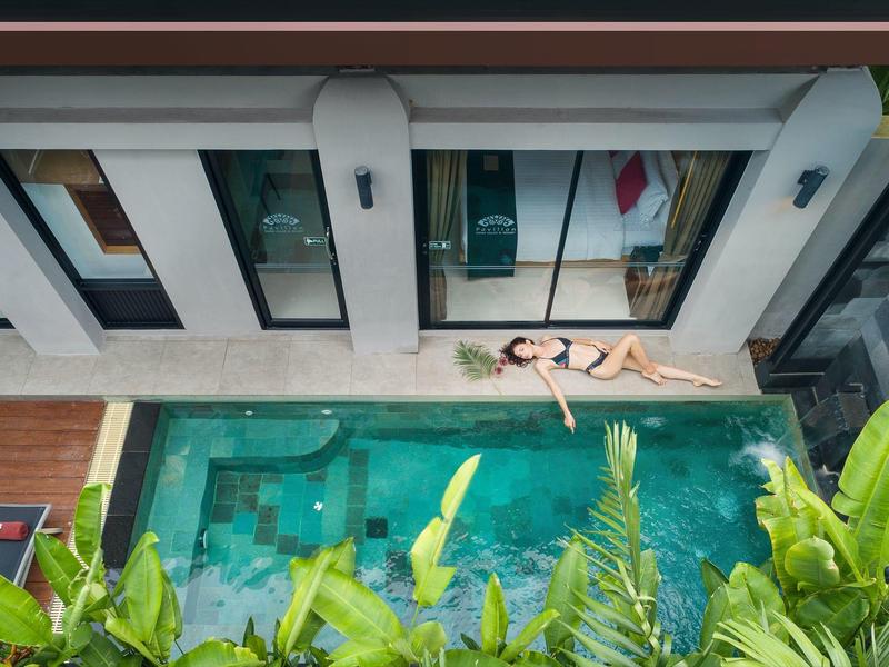 Vista dall'alto di una piscina con una persona su una tavola galleggiante accanto a una terrazza moderna con piante.
