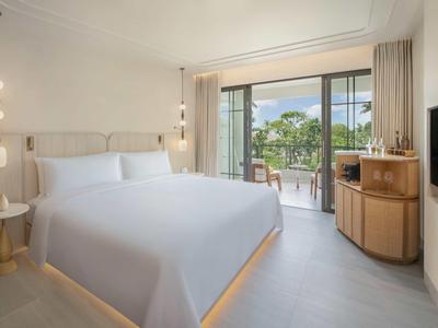 Modernes Hotelzimmer mit großem Bett, Balkon und Blick auf Bäume.