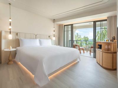 Modernes Hotelzimmer mit großem Bett und Balkon mit Sitzgelegenheit und Gartenblick.
