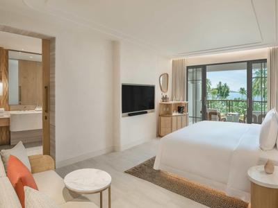 Helles Hotelzimmer mit Doppelbett, Couch, TV und Balkon mit Seeblick.