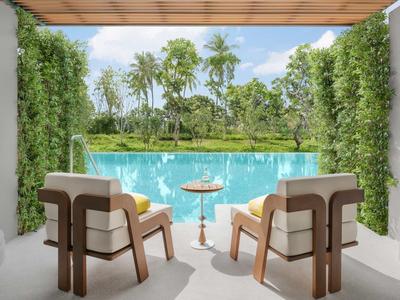 Zwei bequeme Stühle und ein Tisch mit Getränken auf einer Terrasse mit Blick auf einen Pool und Palmen.