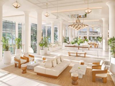 Heller, moderner Hotellobby mit weißen Säulen, bequemen Sitzgelegenheiten und großen Fenstern mit Blick ins Freie.