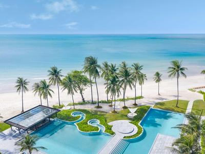 Blick auf einen tropischen Pool mit Palmen und Meer im Hintergrund bei klarem Himmel.