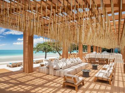 Offener Strandloungebereich mit Holzstruktur, Hängematten und Blick aufs Meer unter blauem Himmel.