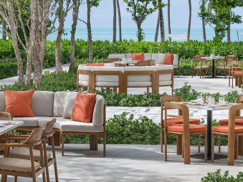 Moderner Außenbereich mit Holzstühlen, Sofas, orange Kissen und grüner Bepflanzung.