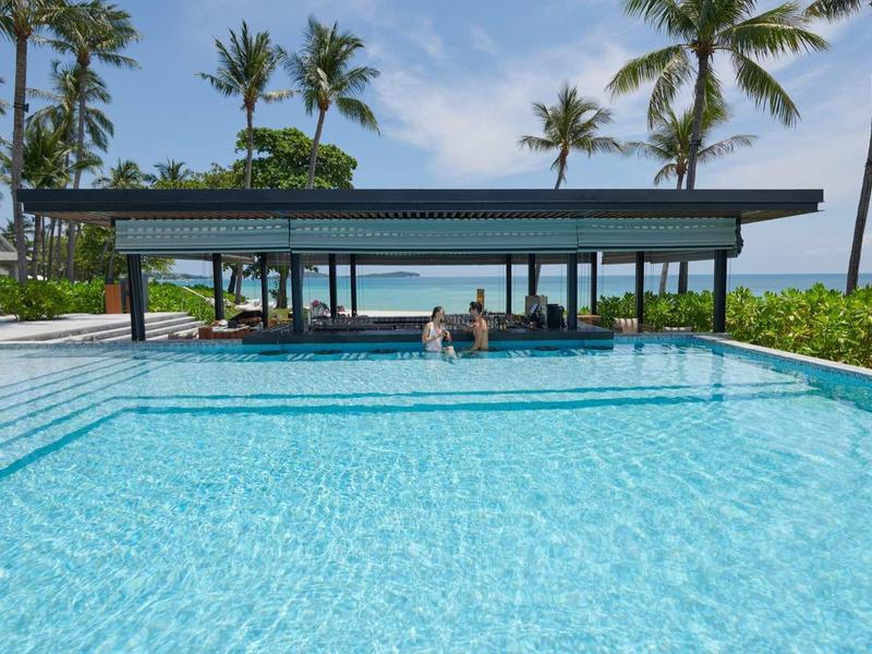 Großer Infinity-Pool mit Bar unter Palmen in tropischem Resort bei klarem Himmel.