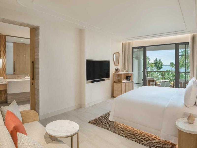 Helles Hotelzimmer mit Doppelbett, Couch, TV und Balkon mit Seeblick.