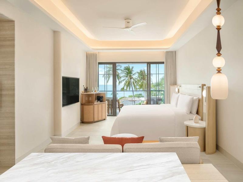 Modernes Hotelzimmer mit Doppelbett, TV, Deckenventilator und Meerblick durch große Fenster