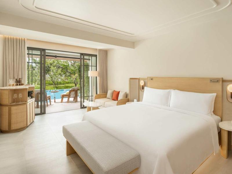 Modernes Hotelzimmer mit großen Fenstern, Doppelbett und Blick auf Terrasse und Garten.