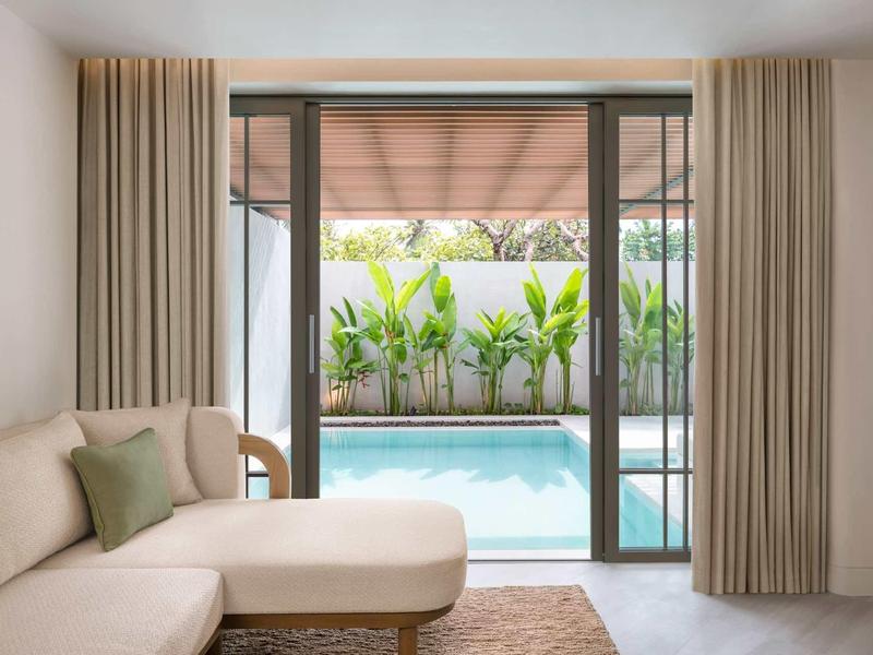 Modernes Wohnzimmer mit beigem Sofa und Blick auf privaten Pool durch große Glasschiebetüren.