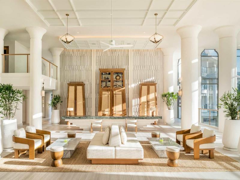 Helles, modernes Wohnzimmer mit weißen Möbeln, hölzernen Tischen, Pflanzen und großen Fenstern.