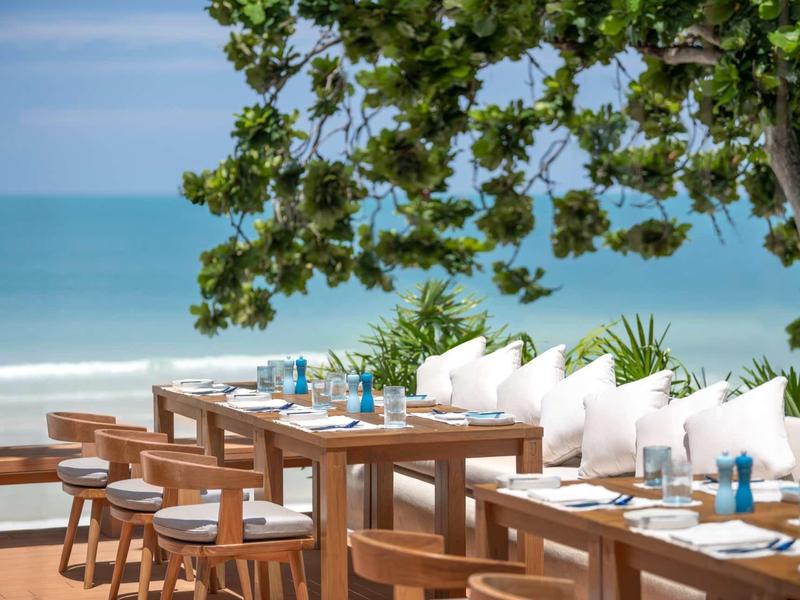 Strandrestaurant mit Holzmöbeln und Meerblick bei klarem Himmel.
