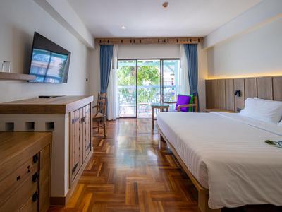 Helles Hotelzimmer mit Doppelbett, Schreibtisch, Fernseher und Balkon mit Blick auf Grün.