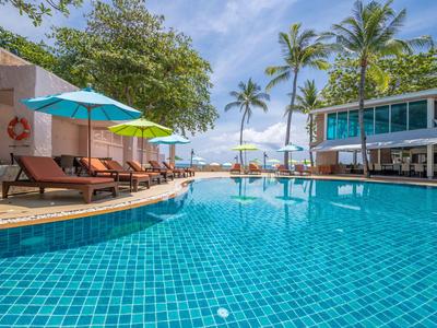 Hotelpool mit Liegestühlen, Sonnenschirmen und Palmen unter blauem Himmel.