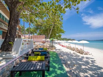 Pláž s stoly, židlemi a slunečníky u hotelu s jasnou oblohou a tyrkysovou vodou.