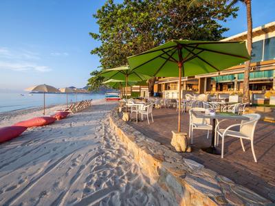 Plážová restaurace s bílými stoly a zelenými slunečníky vedle písku a moře