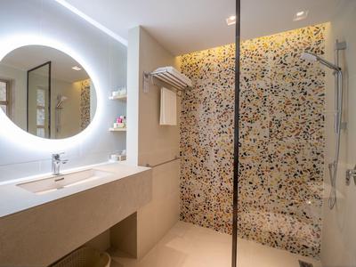 Moderní koupelna s osvětleným zrcadlem, umyvadlem a barevnou mozaikovou sprchou.