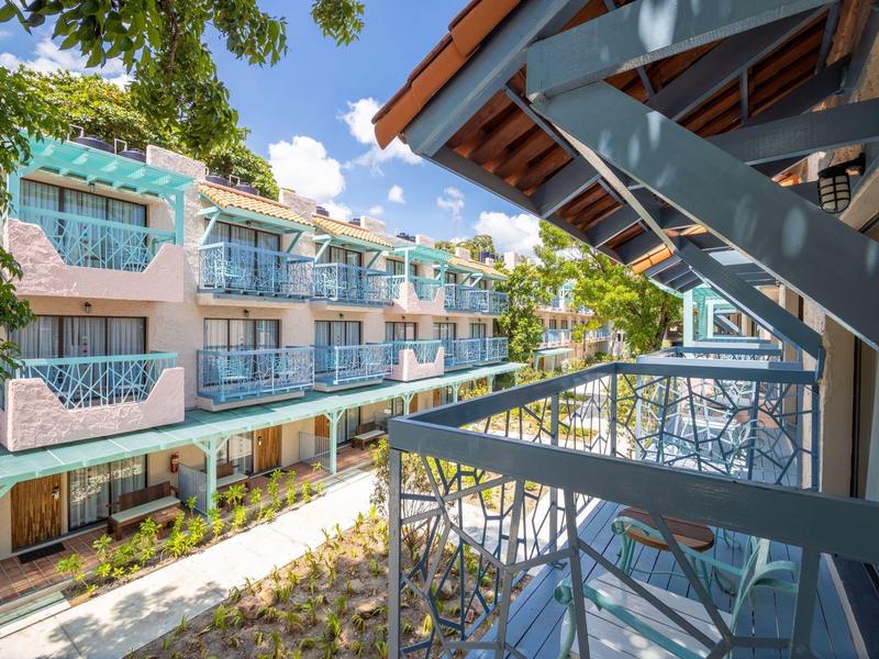 Pohled z balkonu na moderní hotelovou budovu se skleněnými zábradlími a modrými akcenty.