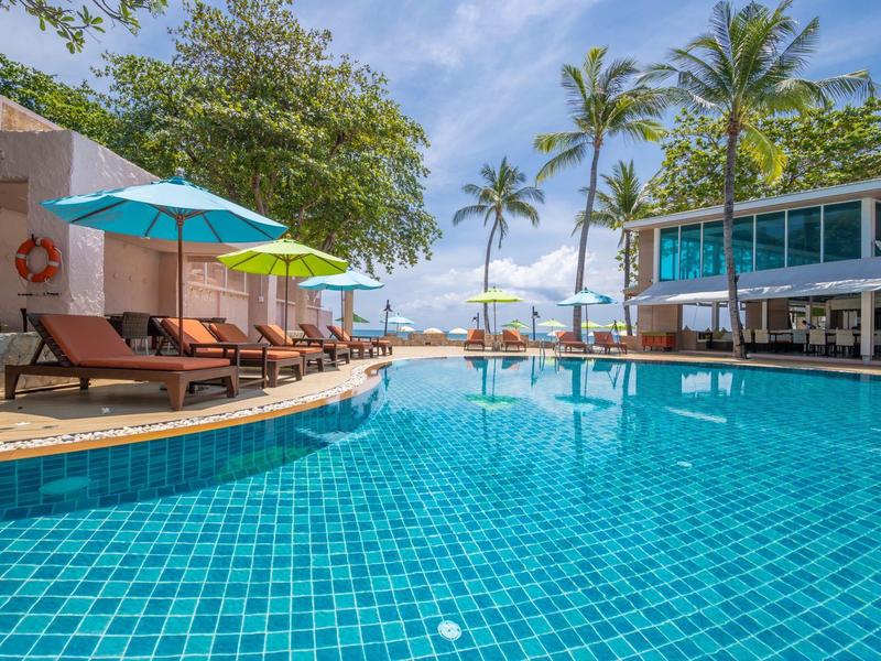 Venkovní bazén s lehátky, slunečníky a palmami pod modrou oblohou.