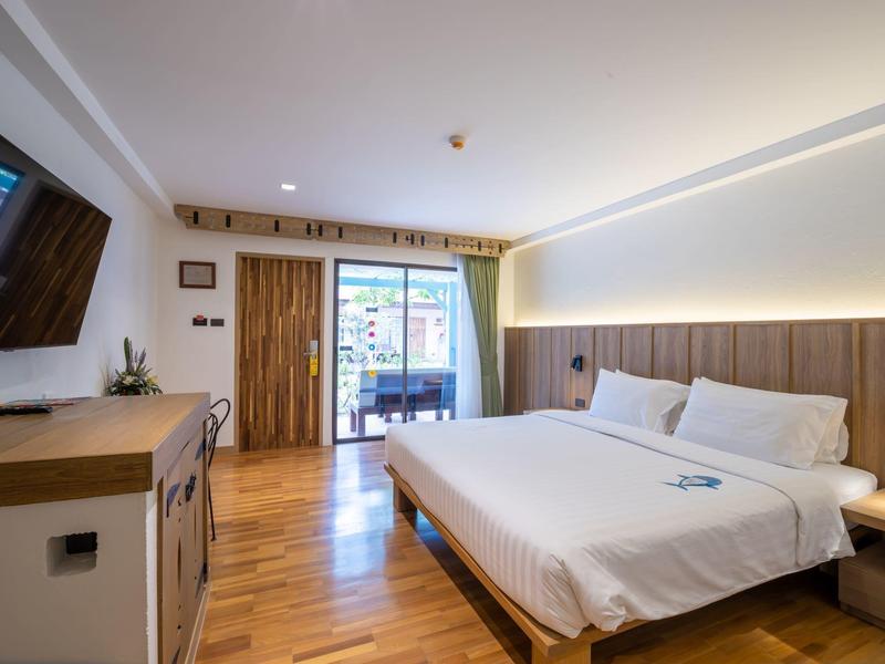 Moderní hotelový pokoj s velkou postelí, dřevěnou podlahou a balkonem s výhledem na město.