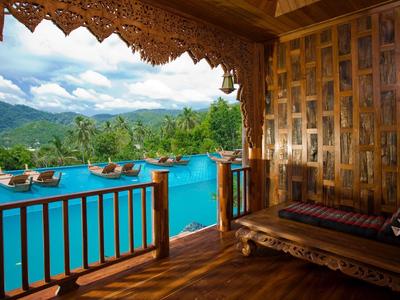 Blick von einer Holzterrasse mit Sitzbereich auf einen Pool und Berge im Hintergrund.