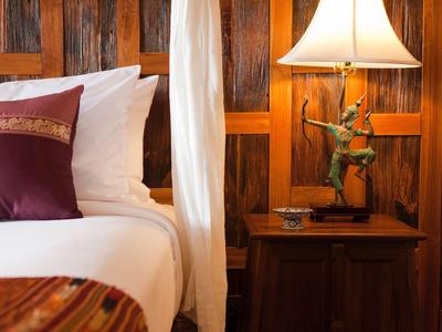 Gemütliche Hotelzimmer-Ecke mit Bett, Kissen, Nachttisch und dekorativer Lampe auf Holzpaneelen.