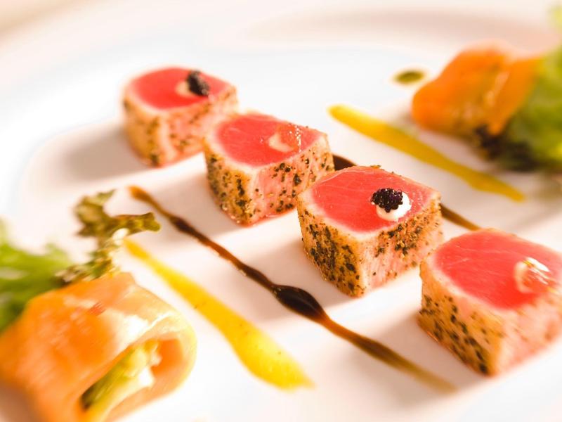 Quadratische Stücke von Sesam-Thunfisch mit Saucen auf einem weißen Teller angerichtet