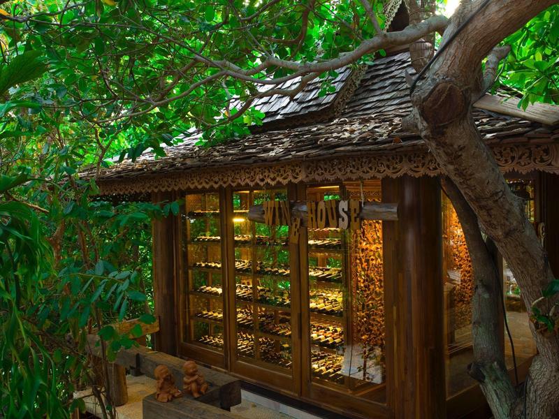 Rustikales Holzgebäude mit großen Fenstern, umgeben von dichtem Grün in einer naturnahen Umgebung.