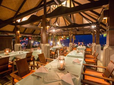 Offenes Restaurant mit Holzstuhlreihen, gedeckten Tischen und warmem Licht bei Nacht.