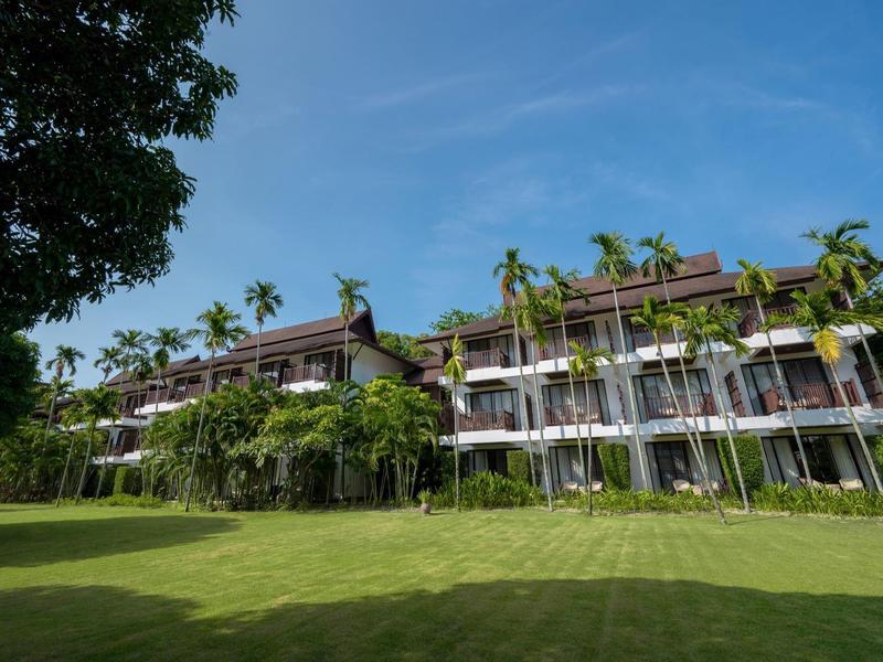 Großes Gebäude mit mehreren Stockwerken, umgeben von grünen Palmen und einem gepflegten Rasen.