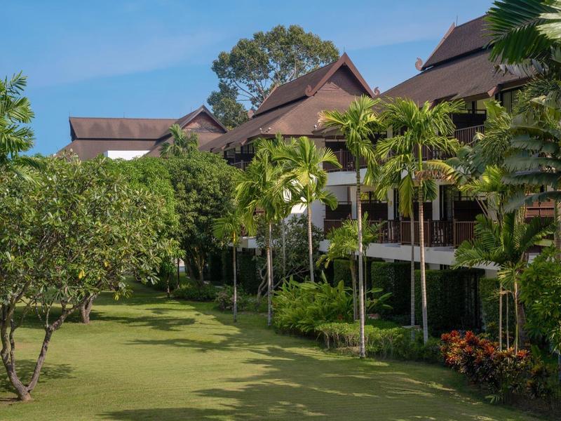 Reihen von Gebäuden mit braunen Dächern und vielen Palmen auf einem großen grünen Rasen.