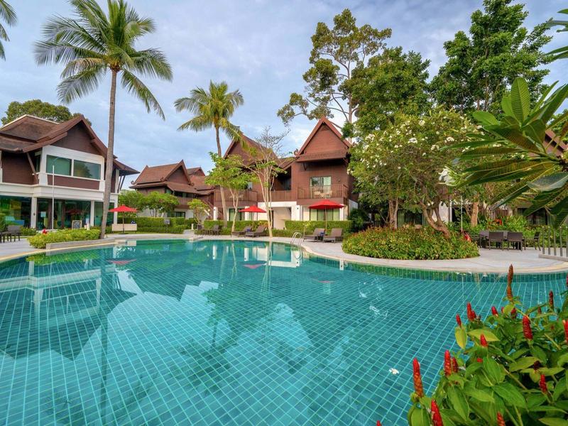 Ein großer Pool umgeben von grünen Pflanzen und tropischen Bäumen neben mehrstöckigen Holzhäusern.