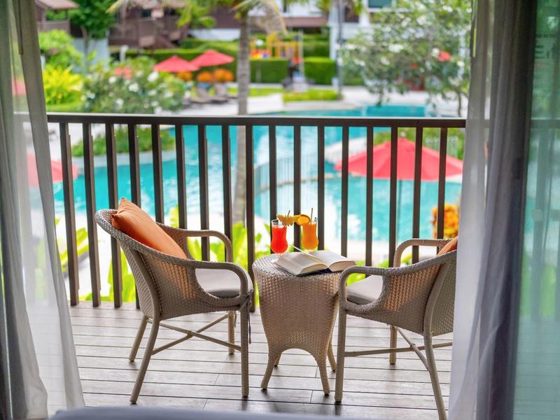 Zwei Stühle und ein Tisch auf Balkon mit Blick auf buntes Schwimmbecken und Garten.