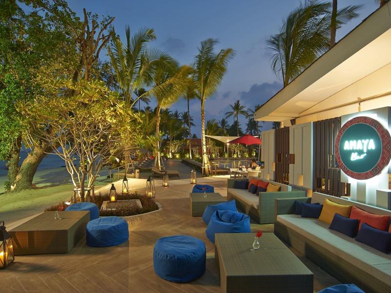 Gemütliche Outdoor-Lounge mit Polstersesseln, blauen Sitzkissen und Palmen bei Abenddämmerung.