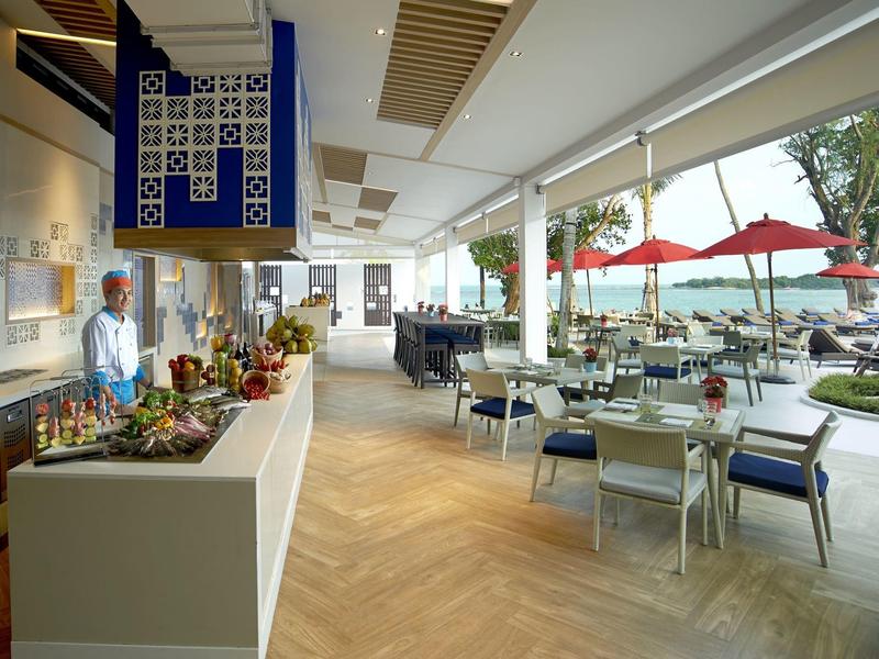 Modernes Restaurant mit Holzfußboden, weißen Tischen, blauen Stühlen und großer Glasfront zum Außenbereich.