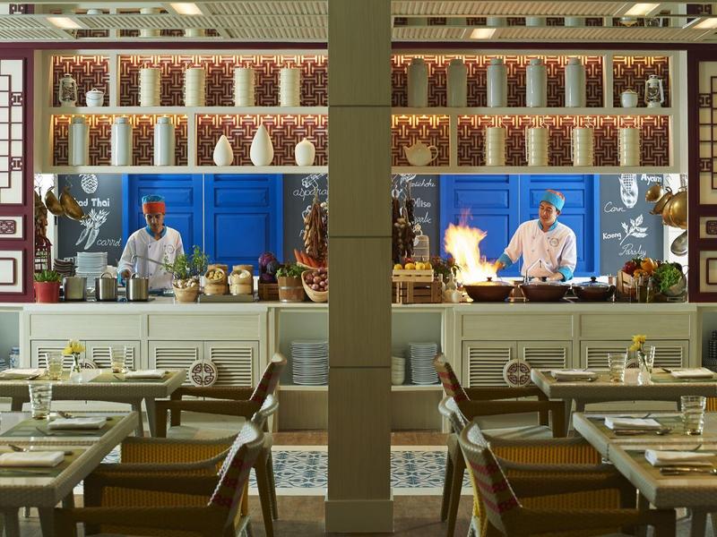 Modernes Restaurant mit gedeckten Tischen, Glasvasen und zwei Köchen in offener Küche.