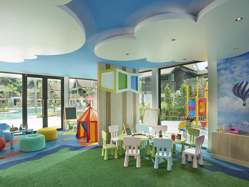 Hell eingerichteter, bunter Kinderspielraum mit Teppichboden, kleinen Tischen, Stühlen und großer Fensterfront.