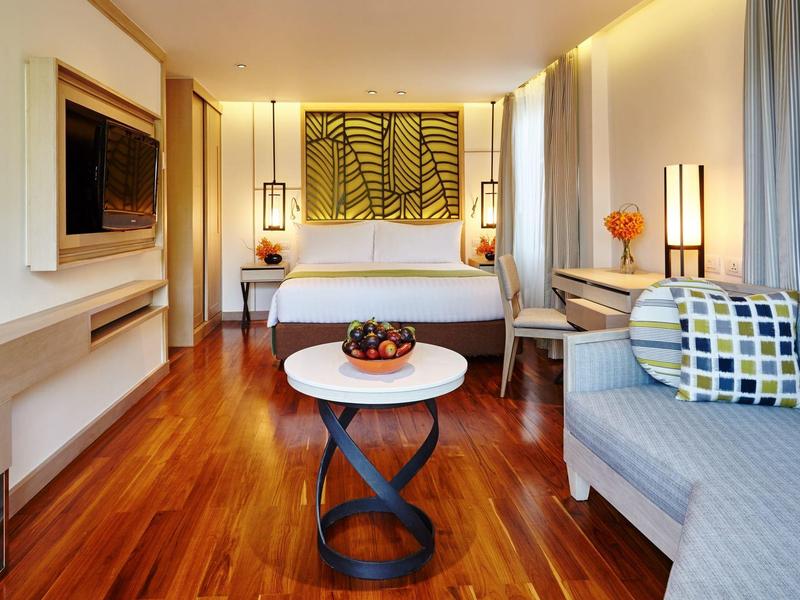 Modernes Schlafzimmer mit Holzboden, grauem Sofa, rundem weißen Tisch und großem Bett mit dekorativem Kopfteil.