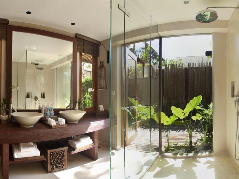 Helles Badezimmer mit Holzmöbeln, Glasdusche und großer Fensterfront mit Pflanzen draußen.