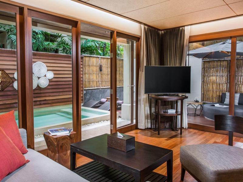 Gemütliches Wohnzimmer mit Holzmöbeln, rotem Kissen und Blick auf Terrasse mit Pool und Garten.