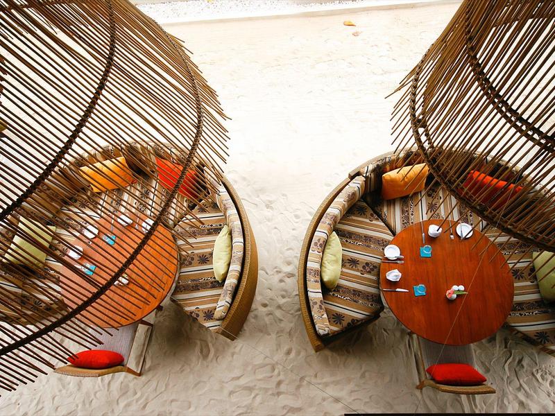 Zwei runde Sitzbereiche mit Holztisch und Polstern, überdacht von geflochtenen Schirmen am Strand.