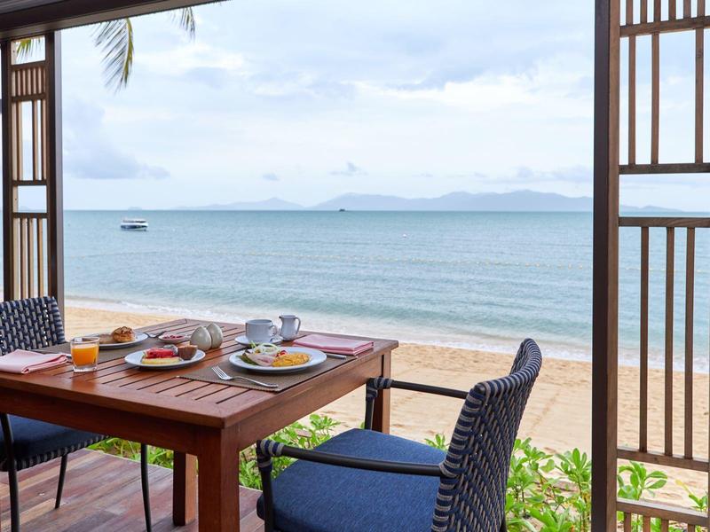 Ein gedeckter Tisch auf einer Terrasse mit Blick auf einen Sandstrand und das Meer.