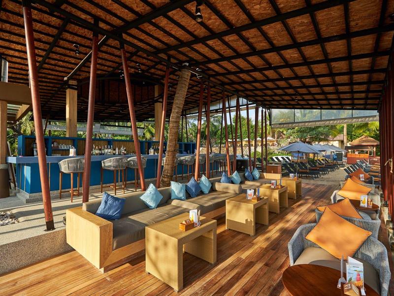 Offene Lounge mit Holzmöbeln und Bar in tropischer Hotelumgebung