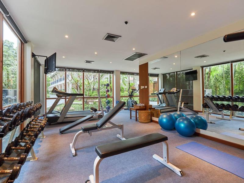 Heller moderner Fitnessraum mit Hanteln, Laufbändern, Bänken und Gymnastikbällen vor großen Fenstern.