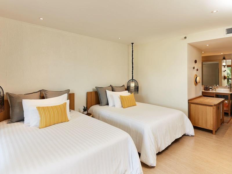 Hotelzimmer mit zwei Doppelbetten, modernem Holzfußboden und warmen Beleuchtungskörpern.